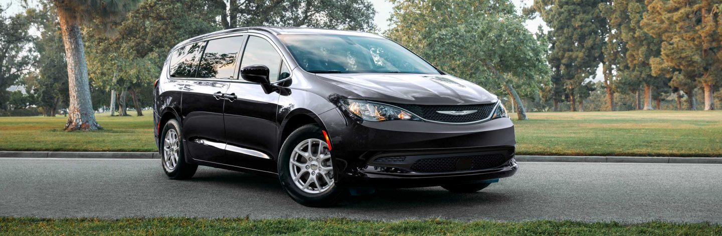 A three-quarter profile of the 2022 Chrysler Voyager on a road running through a park.