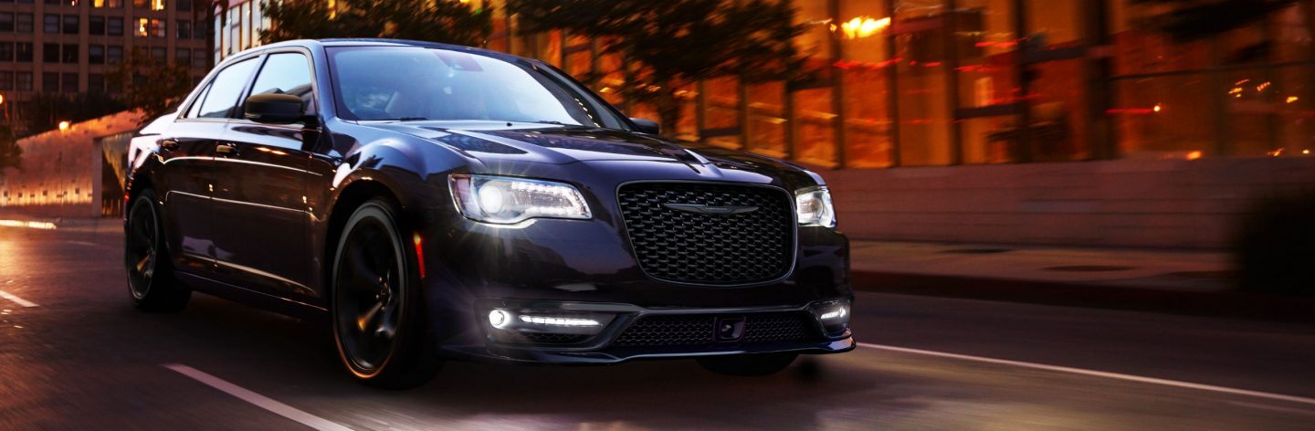 A 2023 Chrysler 300S with its headlamps on, being driven on a city street at night.
