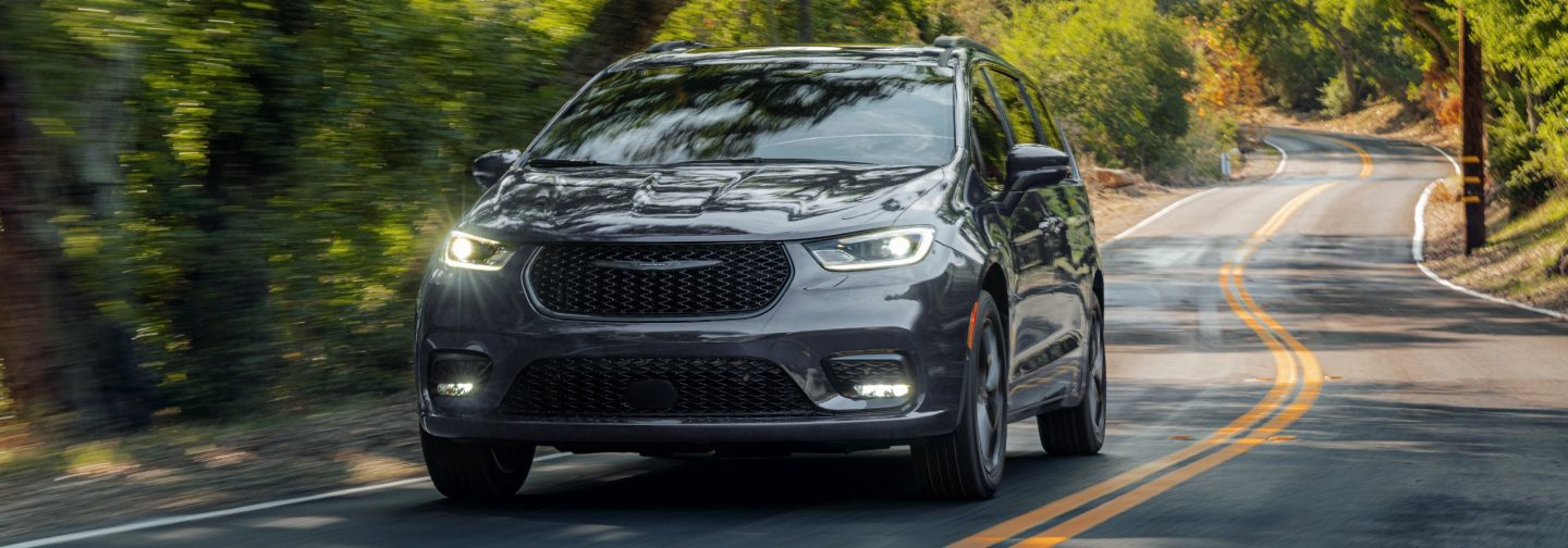 A gray 2026 Chrysler Pacifica Limited traveling down a winding highway in the woods.