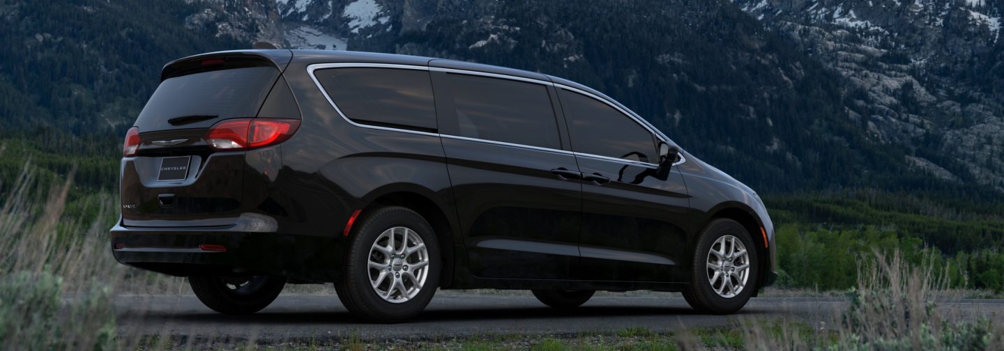A passenger-side rear angle of a black 2026 Chrysler Voyager LX with mountains in the background.