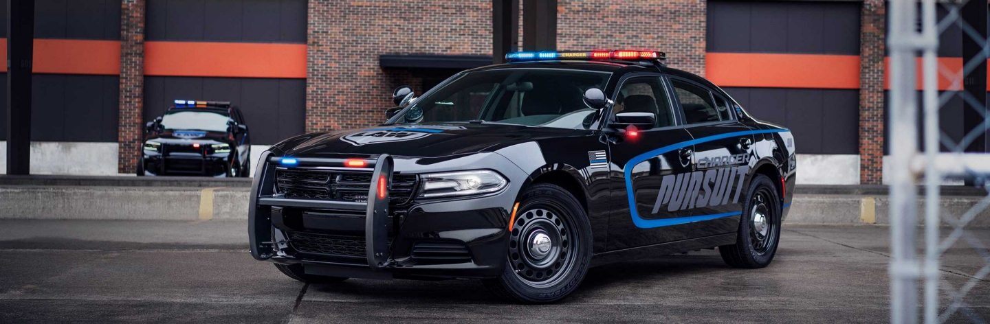 The 2023 Dodge Charger Pursuit with its flasher front end and beacon lights on, parked outside an industrial building.