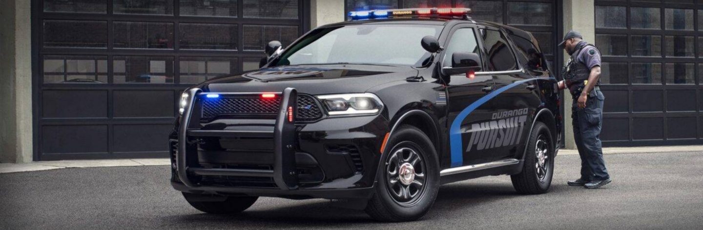 The 2023 Dodge Durango Pursuit AWD with its flasher front end and beacon lights on, parked outside an industrial garage.