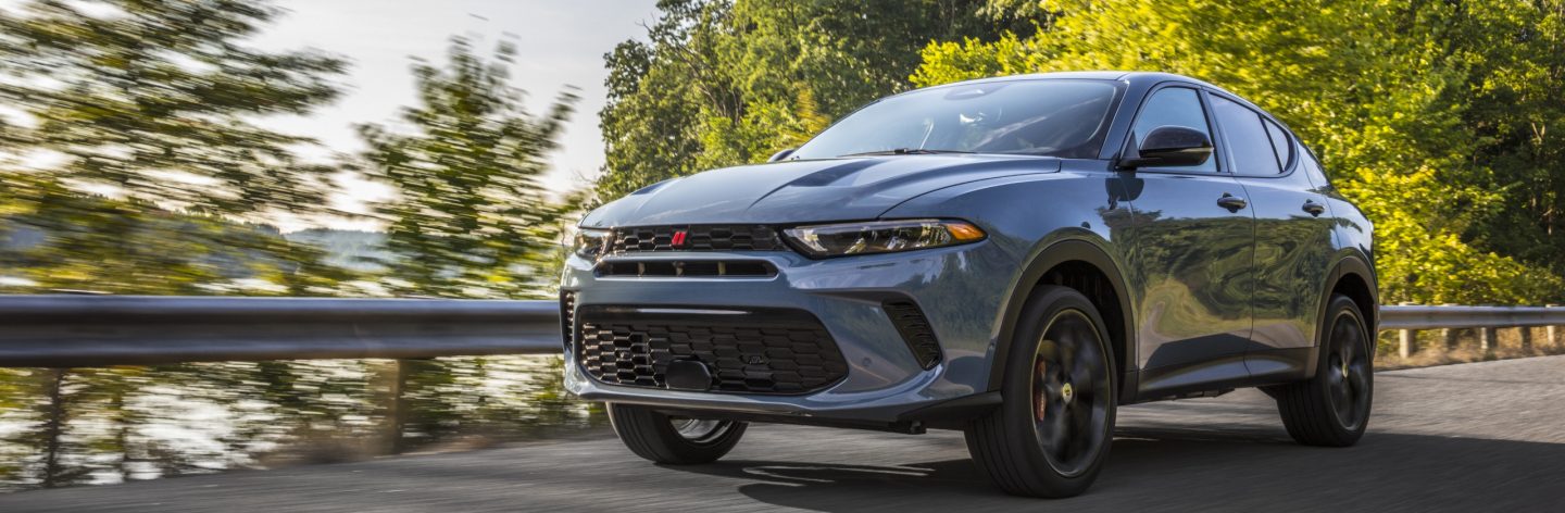 A blue 2024 Dodge Hornet GT being driven on a highway. The background is blurred to indicate the vehicle is in motion.