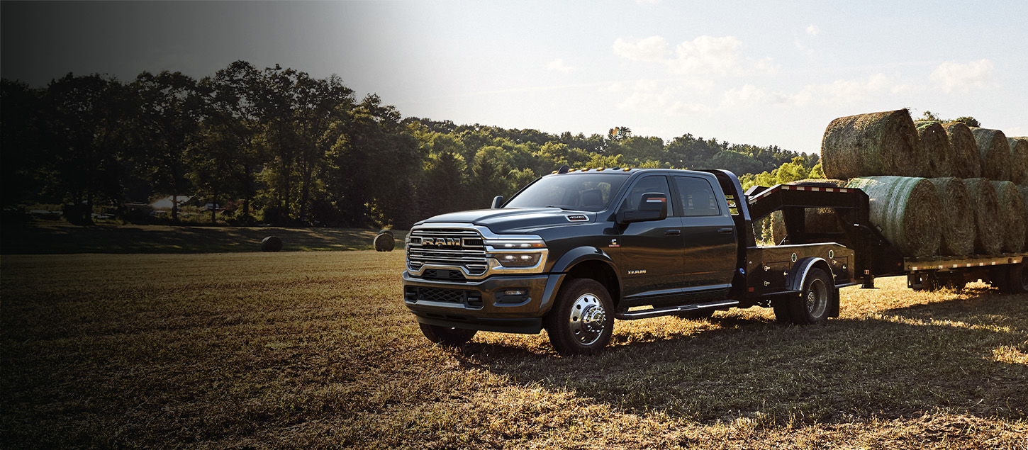 A black 2026 Ram 4500 Big Horn Chassis Cab Crew Cab with the Laramie Trim Group, in an open field, towing several bales of hay with a gooseneck trailer.