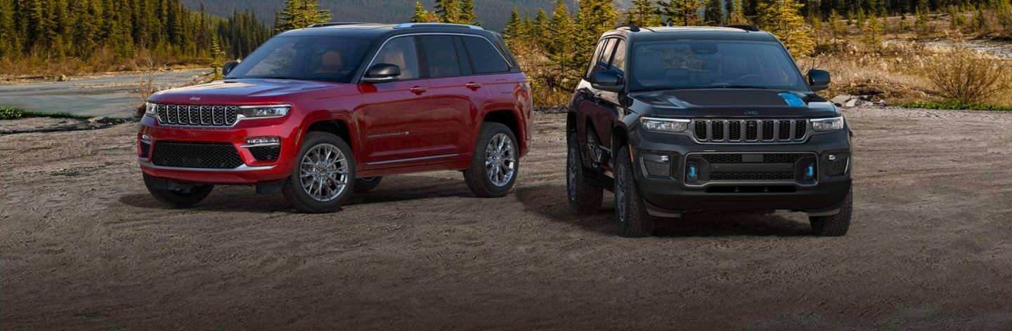 A red 2022 Jeep Grand Cherokee Summit and black Grand Cherokee Trailhawk 4xe parked at a mountain lookout.