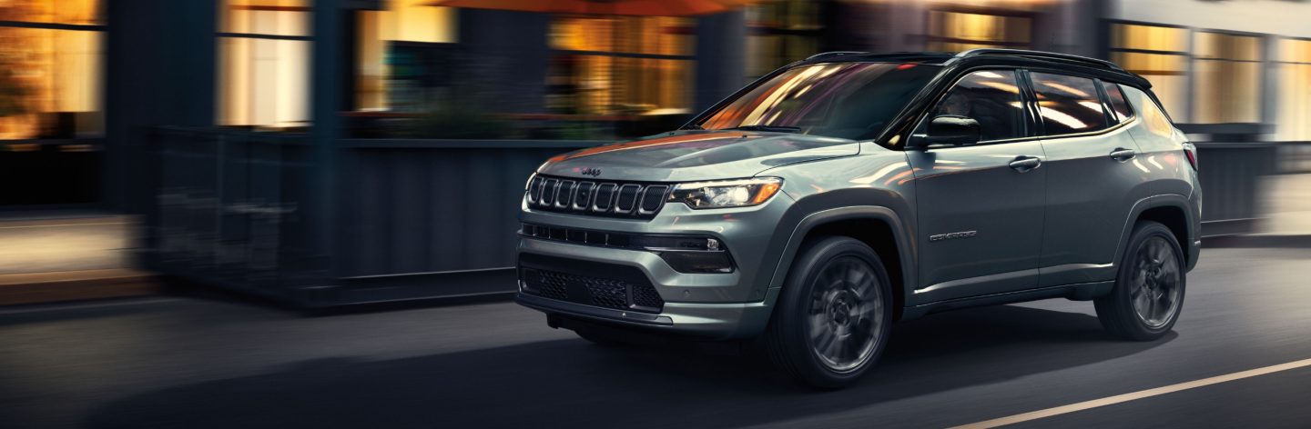 A 2023 Jeep Compass High Altitude being driven on a city street at night, with the background blurred to indicate the vehicle is in motion.