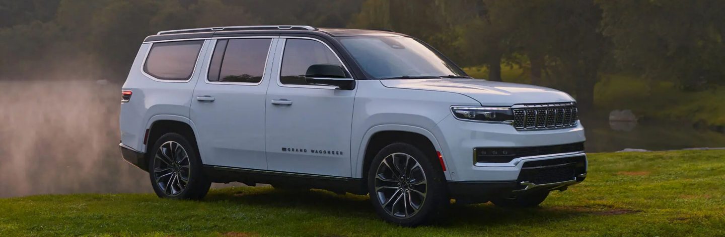 A white 2023 Grand Wagoneer Series III parked on the grass beside a pond with a blanket of fog rising from it.