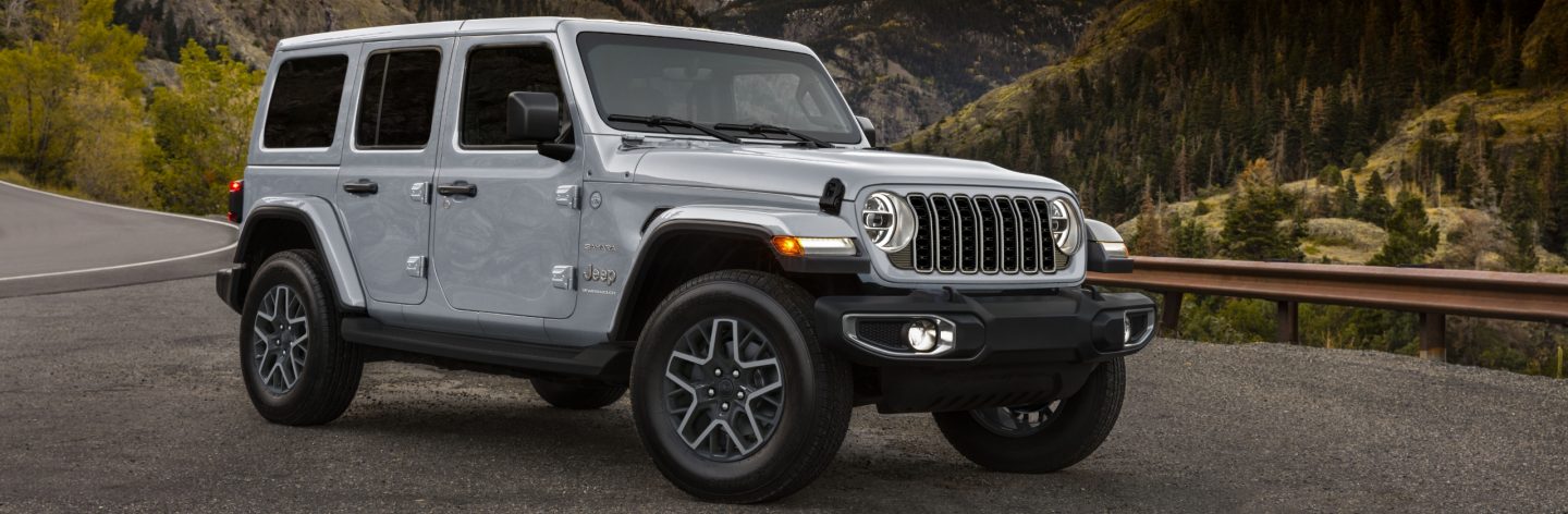 A silver 2024 Jeep Wrangler Sahara parked at a mountain lookout.