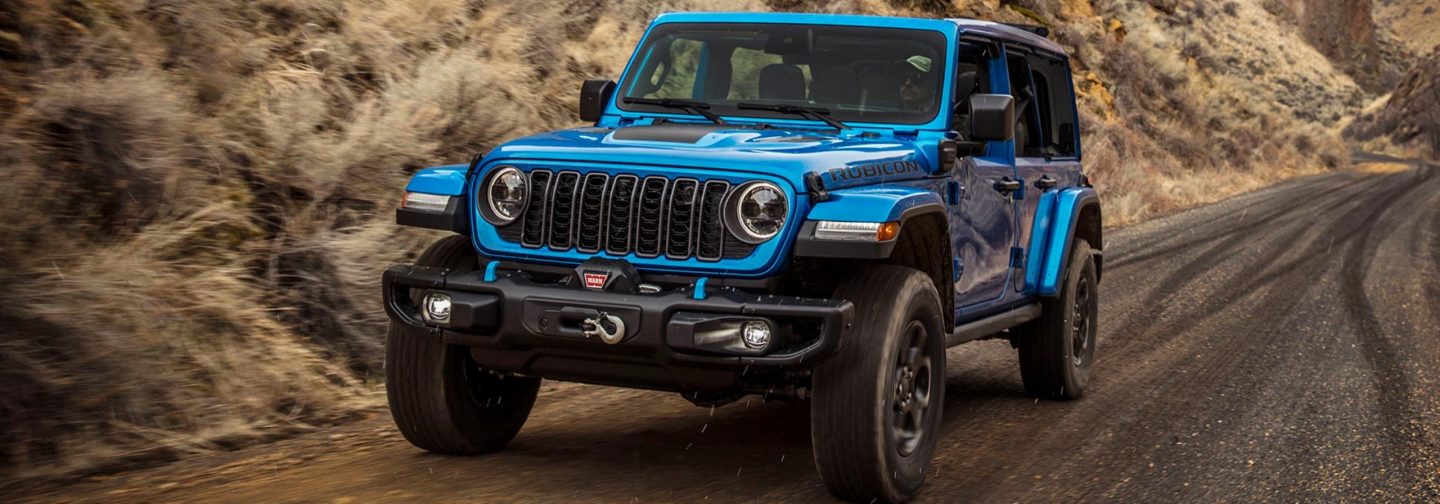 A blue 2025 Jeep Wrangler Rubicon X 4xe traveling on a mountain road.