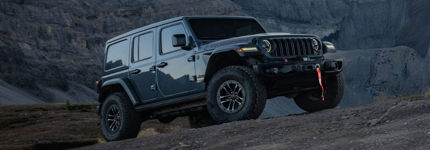 A blue 2025 Jeep Wrangler Rubicon X 4xe traveling on a mountain road.