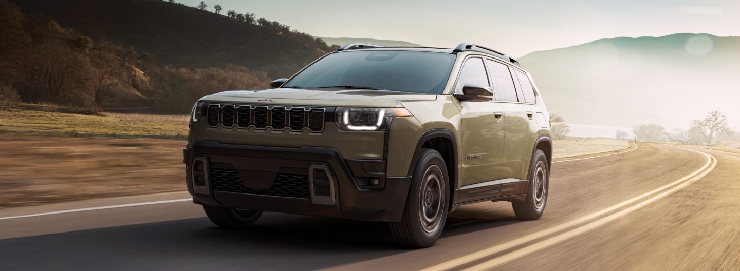 An olive green 2026 Jeep Cherokee Limited traveling down a curved highway.