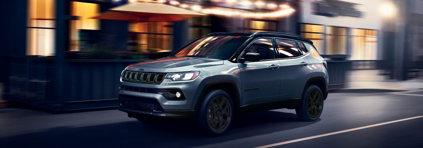 A silver 2026 Jeep Compass Limited Altitude traveling on a city street at night, with the background blurred to indicate the vehicle is in motion.