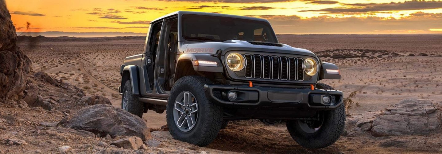 A passenger-side front angle of a red 2026 Jeep Gladiator Rubicon X with its doors and roof removed.