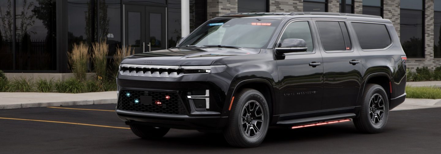 The 2026 Jeep Wagoneer Command Operations Vehicle with its flasher front end lights, beacon lights and side lights on, parked in front of a commercial building.