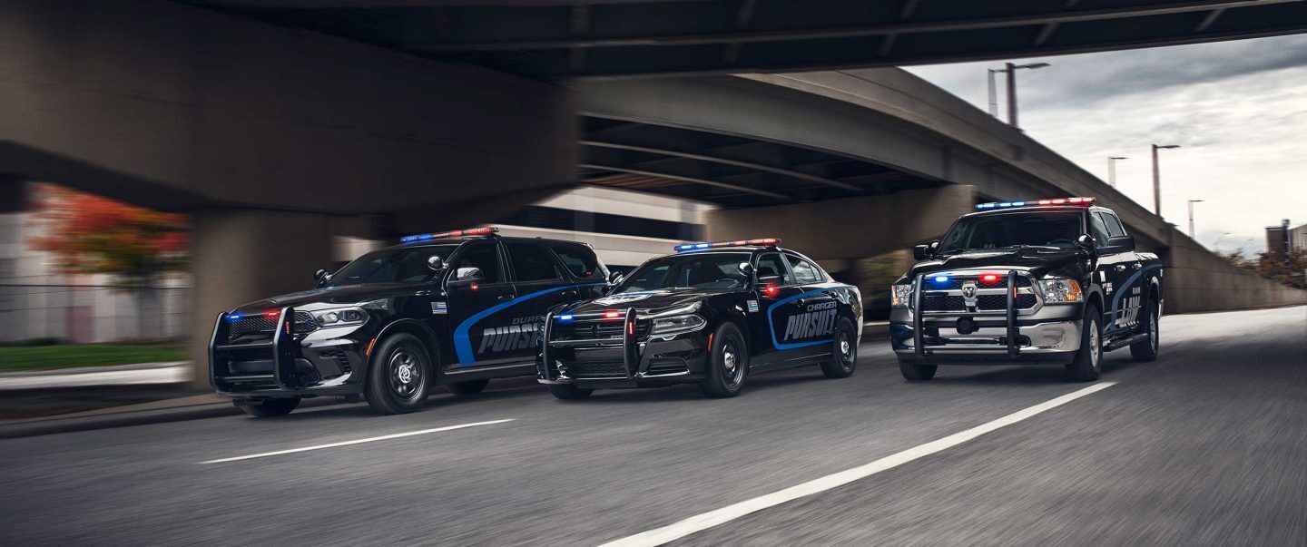 A lineup of the 2022 Dodge Durango Pursuit, Dodge Charger Pursuit and Ram 1500 Classic SSV being driven side-by-side on a highway beside an overpass.