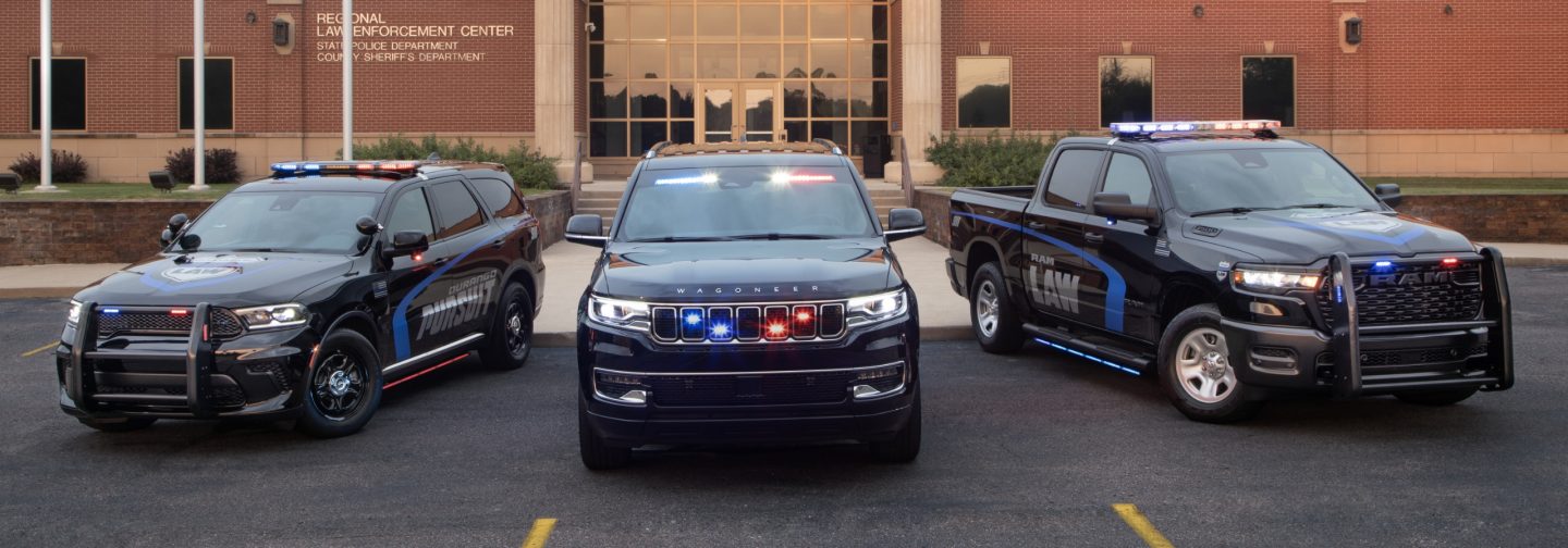 Part of the Stellantis Law Enforcement lineup-- a black 2025 Dodge Durango Pursuit, a black 2025 Jeep Wagoneer Series 1 Special Service Vehicle and a black 2025 Ram 1500 Special Service Vehicle, all parked in the lot of a Reginal Law Enforcement Center with their flasher front end and beacon lights on.
