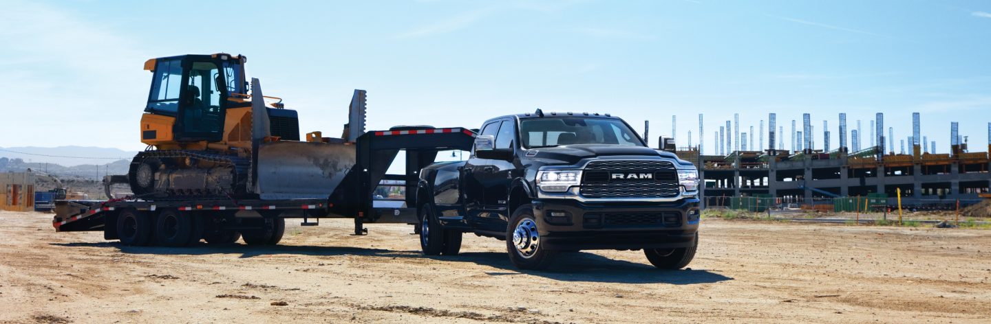 A 2023 Ram 3500 Limited Crew Cab towing a fifth wheel flatbed trailer with an excavator on it.