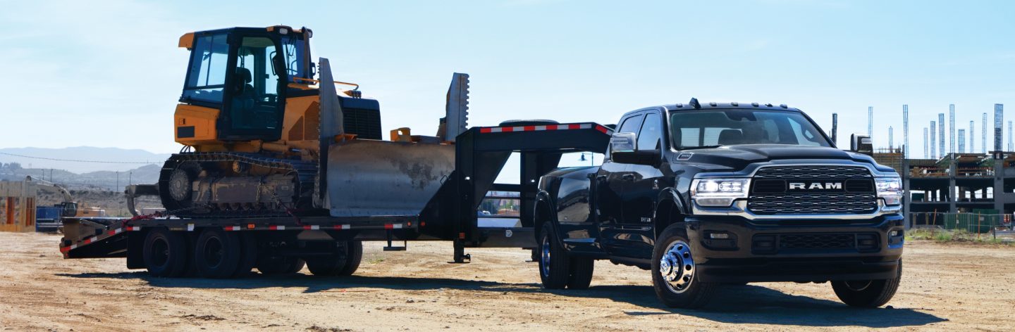 A 2024 Ram 3500 Limited Crew Cab towing a fifth wheel flatbed trailer with an excavator on it.