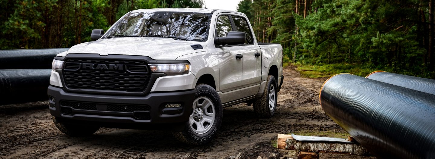 A white 2025 Ram 1500 Tradesman Crew Cab parked at a muddy construction site in the woods.