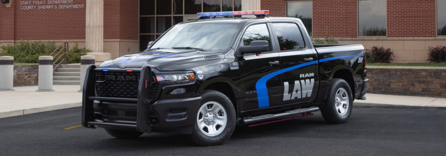 A driver-side front angle of a 2026 Ram 1500 4x4 Crew Cab Special Service Vehicle with its flasher front end lights, beacon lights and side lights on.