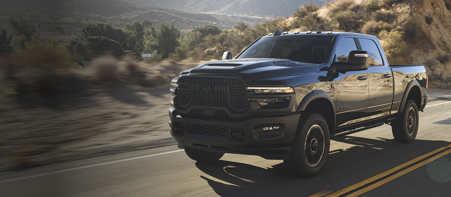 A gray 2027 Ram 2500 Heavy Duty Rebel 4x4 Crew Cab pickup truck traveling down a desert highway.