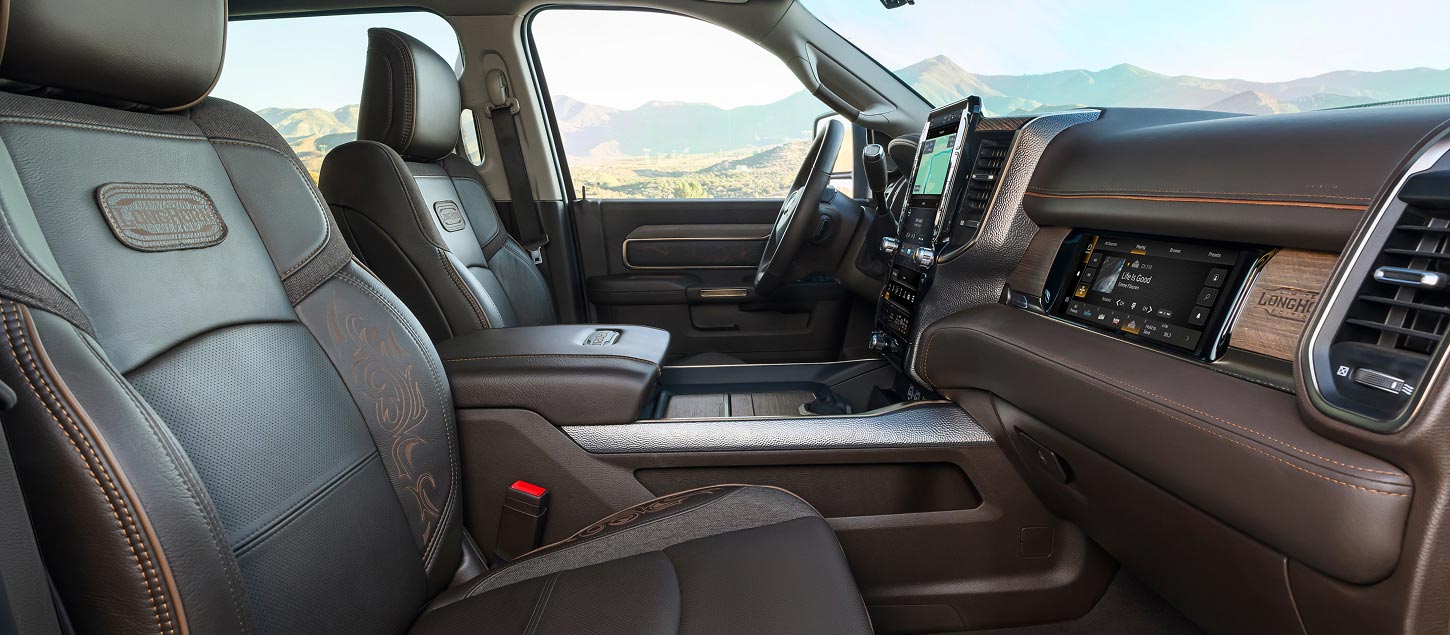 The front seats with an embroidered Limited Longhorn Edition logo on them and the Front Passenger Interactive Display in the 2027 Ram 3500 Heavy Duty Limited Longhorn 4x4 Crew Cab pickup truck. Shot from the passenger side.