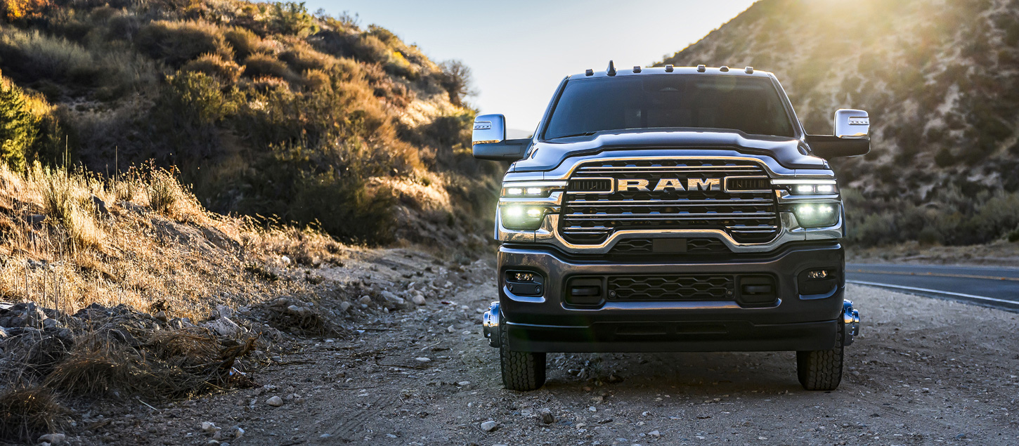 A head-on angle of a black 2027 Ram 3500 Heavy Duty Laramie pickup truck parked on the shoulder of a highway in the mountains.