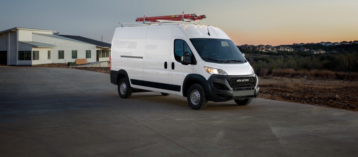 A passenger-side front angle of a white 2027 Ram ProMaster 2500 Tradesman High Roof Cargo Van with a red ladder on its roof rack leaving a construction site.